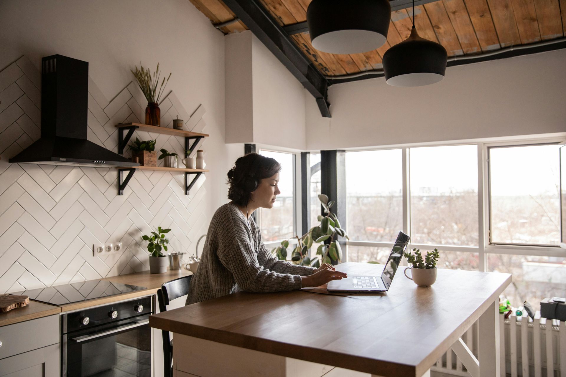 A woman is sitting at a table in a kitchen using a laptop computer.