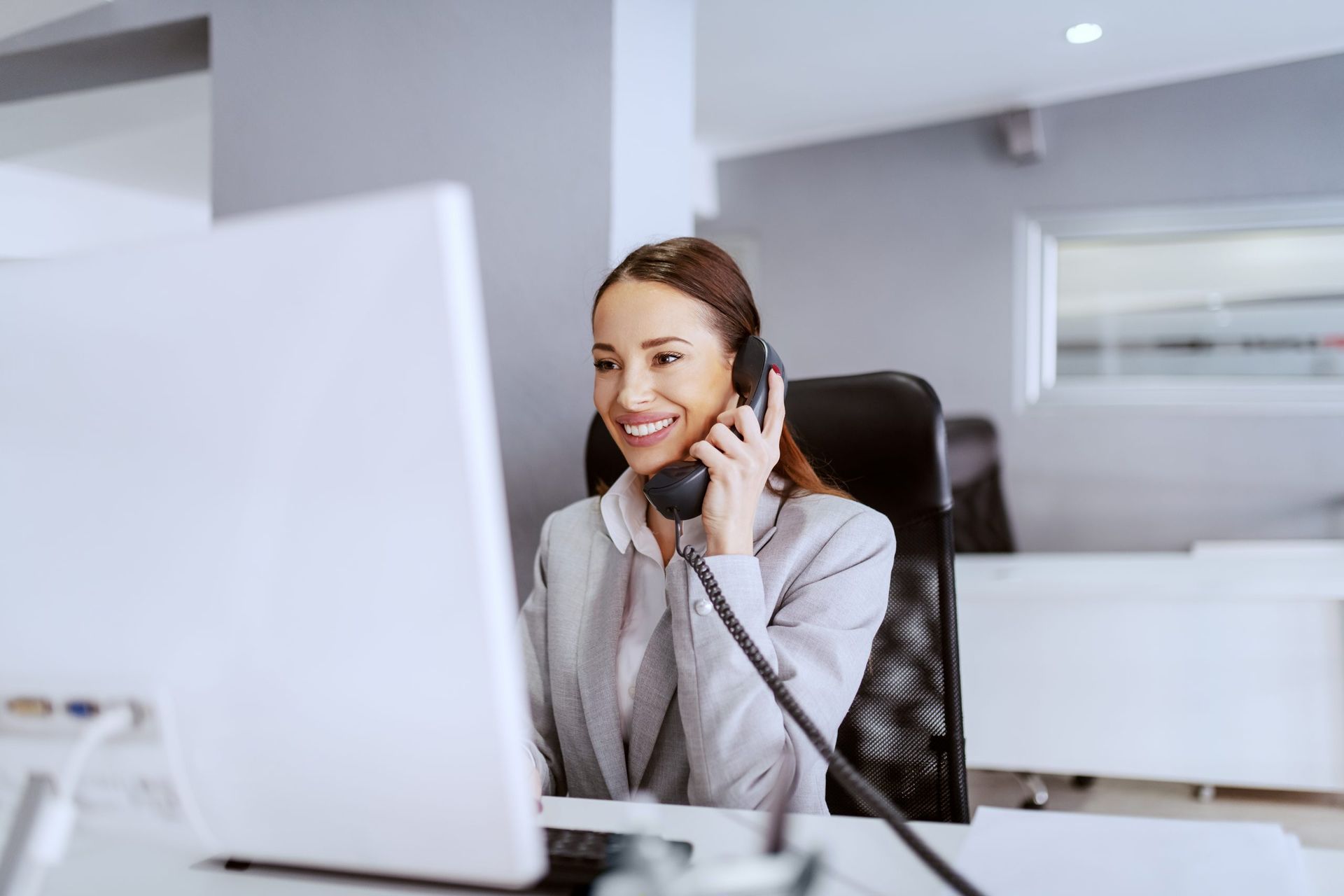 A woman is sitting at a desk in front of a computer talking on a phone.