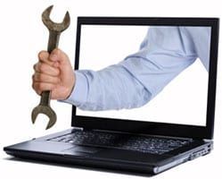 A person is holding a wrench in front of a laptop computer.
