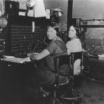A black and white photo of two women sitting at a desk in an office.