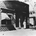 A black and white photo of a woman standing in front of a building.