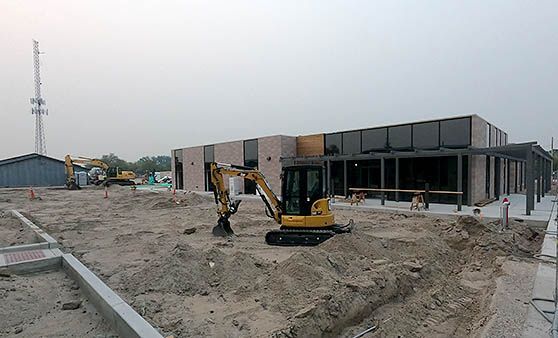 A yellow excavator is digging a hole in front of a building under construction.