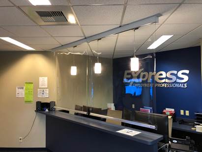 The reception desk of an Express Employment Professionals office with a dark blue counter, glass partition, and wall logo.