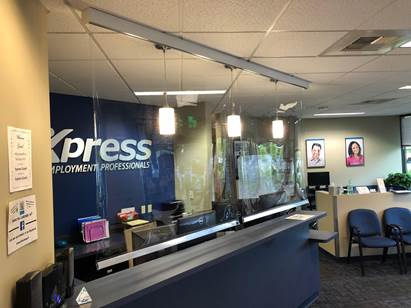 Reception area of an Express Employment Professionals office with a blue logo wall, clear dividers, and a front desk.