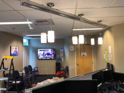 A small office reception area with four pendant lights hanging from the ceiling, a television, and a step ladder.