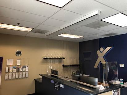 Reception desk at a medical or business office with a dark blue feature wall, an X-shaped logo, and a ceiling-mounted light.