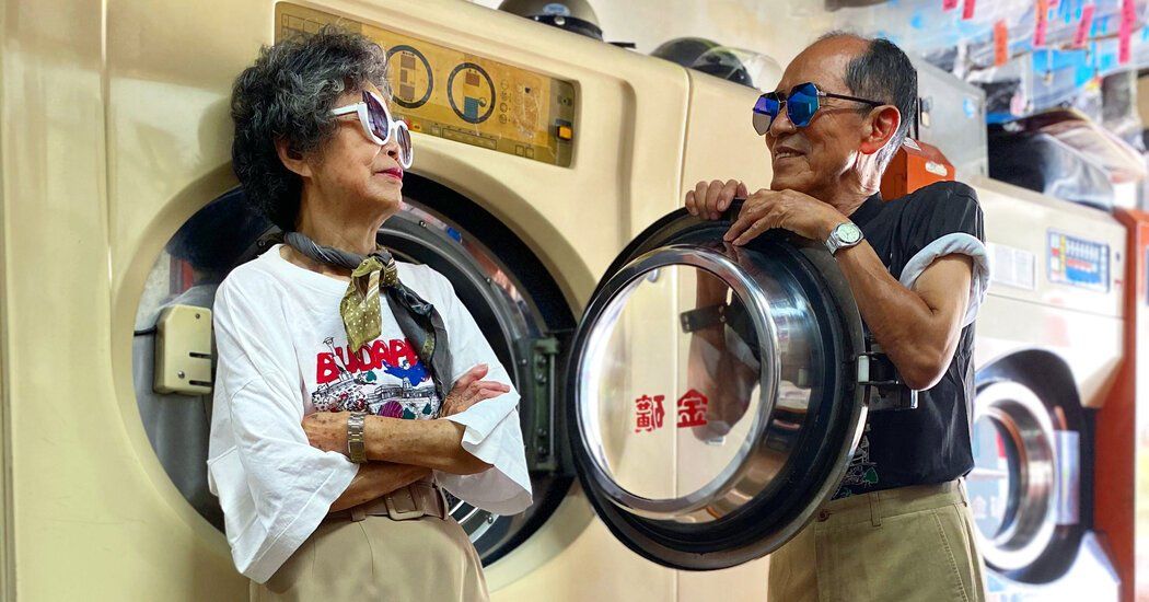 casal idoso posa para foto apoiado em máquina de lavar