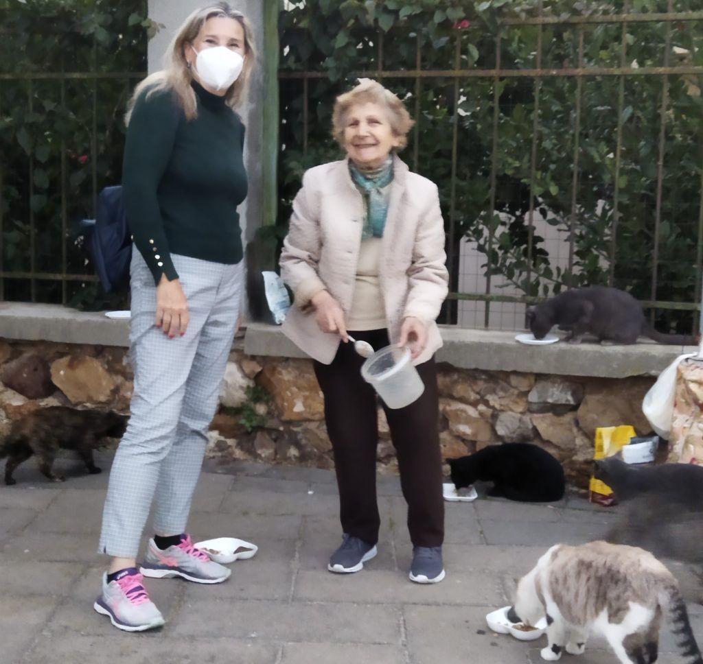 Silvia Triboni, de máscara, posa ao lado de Dorotéia, super sênior de Sardenha que alimenta gatos em situação de rua há 20 anos