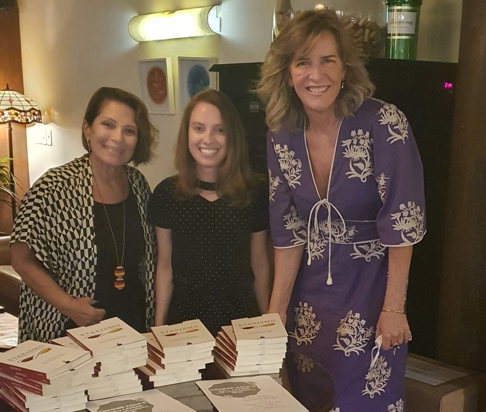 mulheres comemoram o lançamento do livro Etarismo, autora dá autografos para duas leitoras sorridentes. as três mulheres sorriem para a câmera.