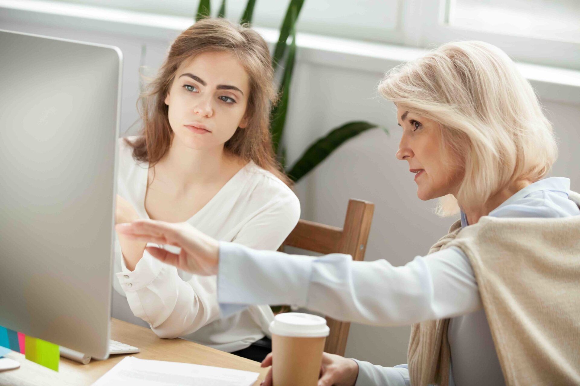 mulher madura mostra algo na tela do computador para mulher mais jovem que olha atentamente