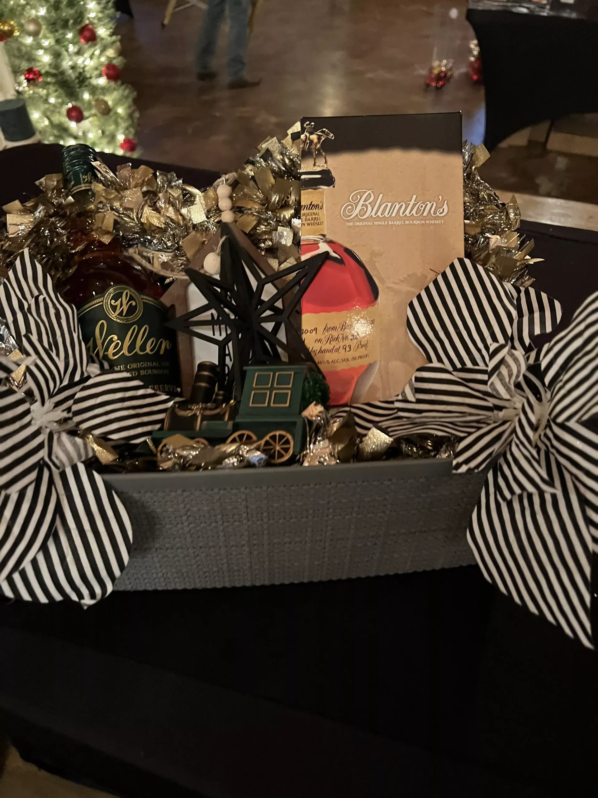 Gift basket with striped bows, holiday treats, and a Christmas tree in the background