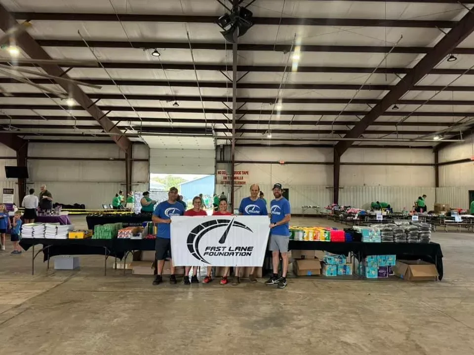 Volunteers behind tables at an indoor food or supply distribution event with a banner in front.