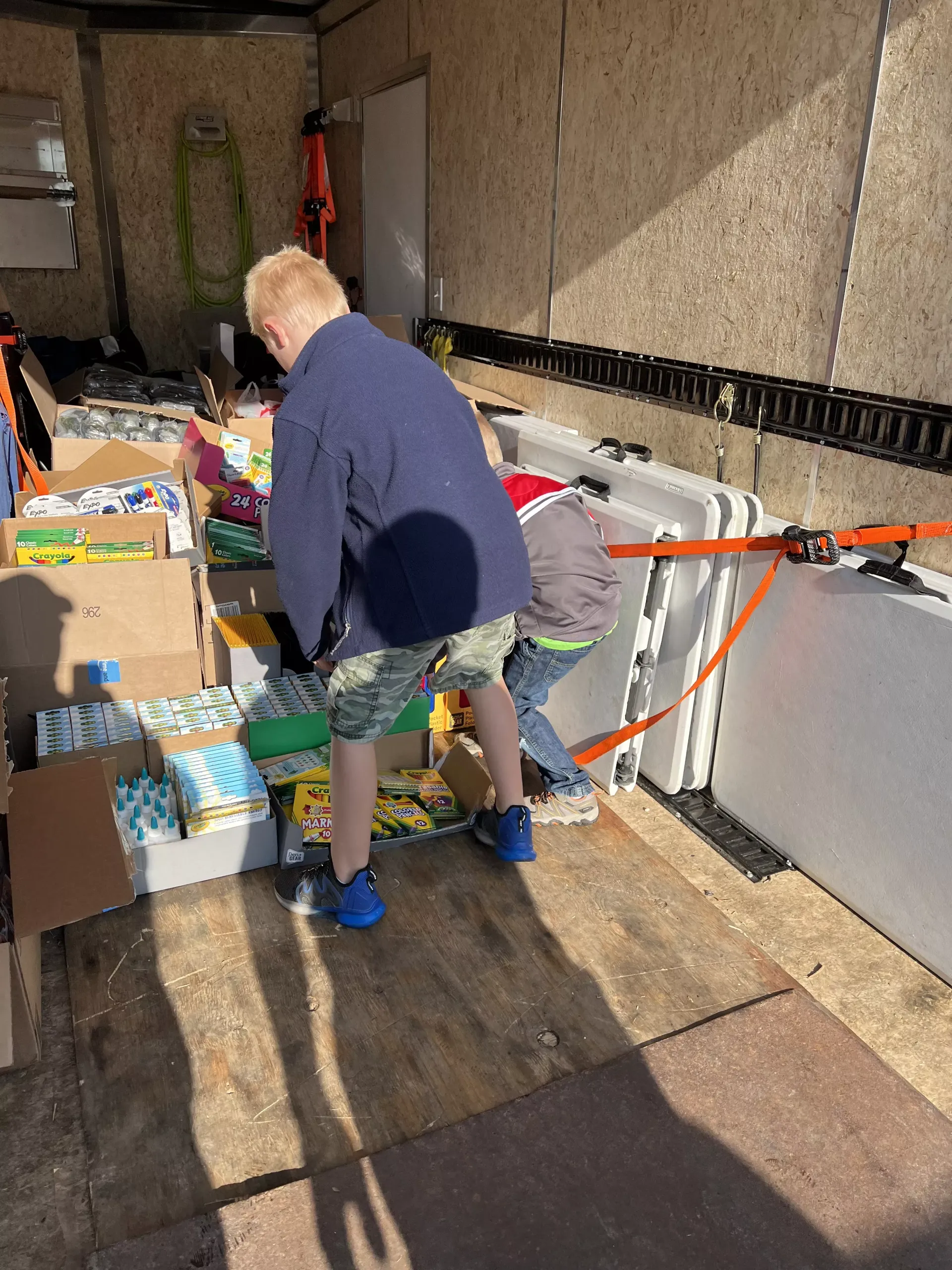 Two people loading boxes into a trailer with orange tie-down straps.