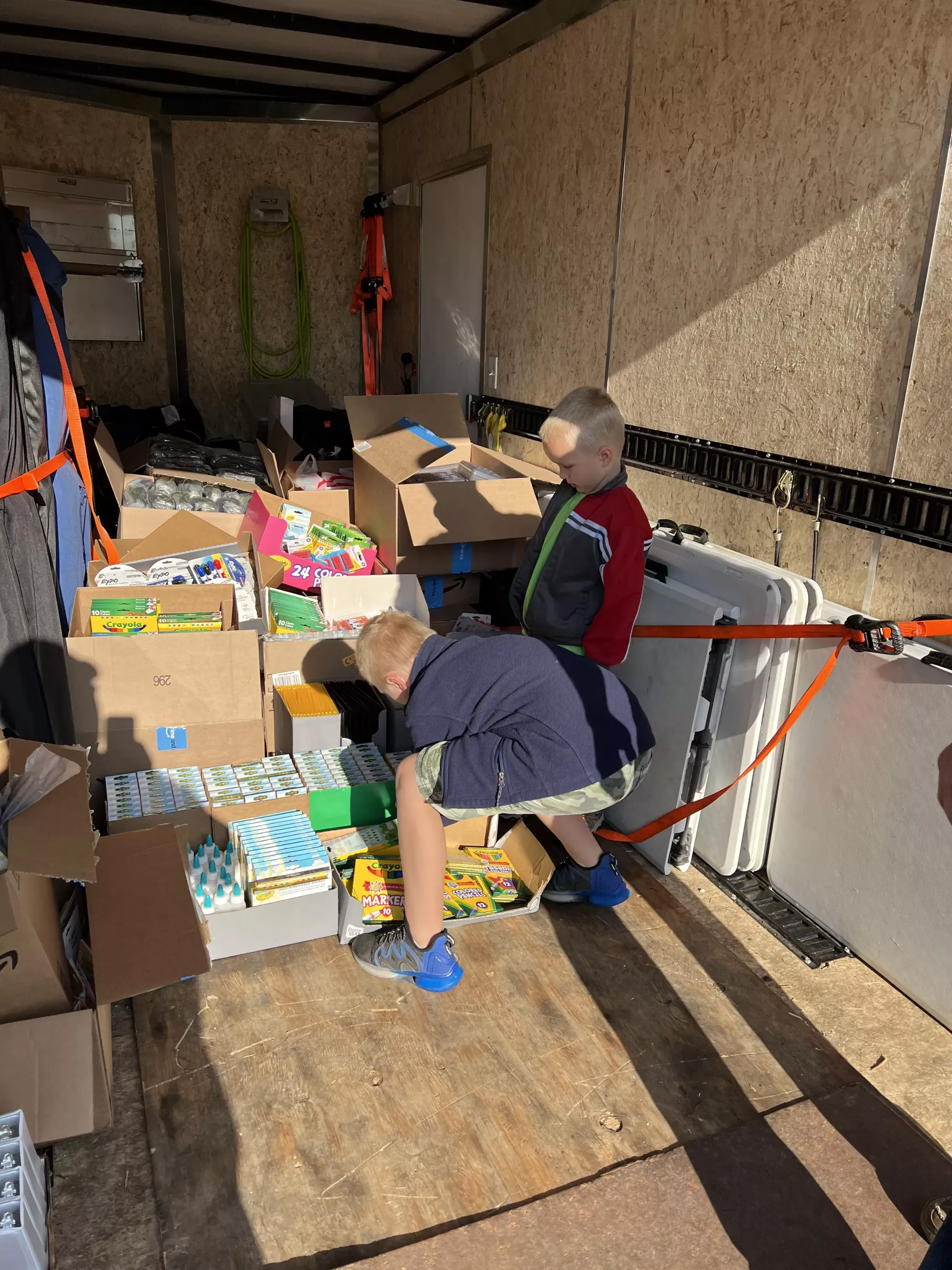 People sorting boxes and supplies inside a moving truck, with cardboard boxes stacked around them.