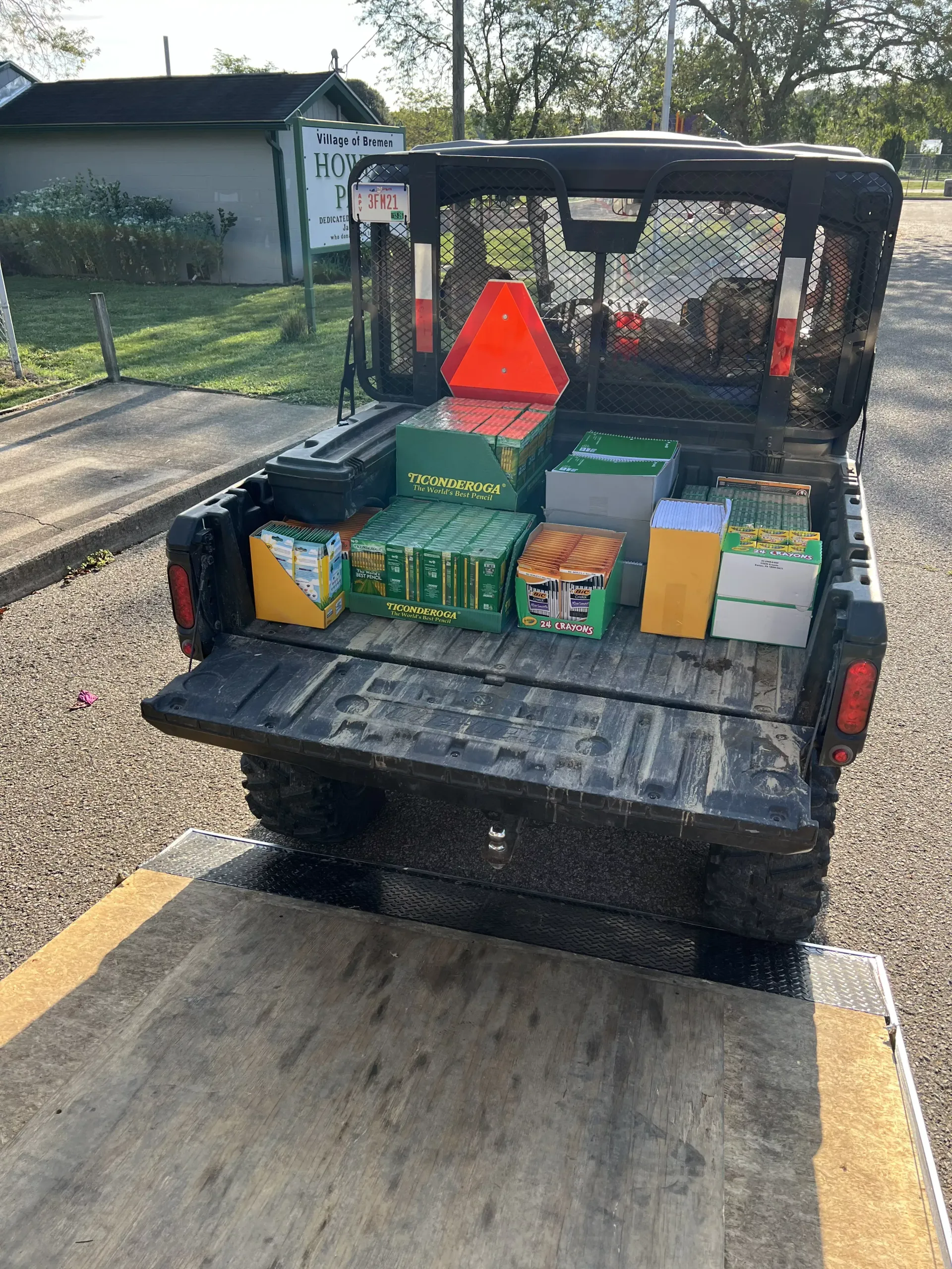 Utility vehicle bed loaded with wrapped packages and a red safety triangle on a driveway.