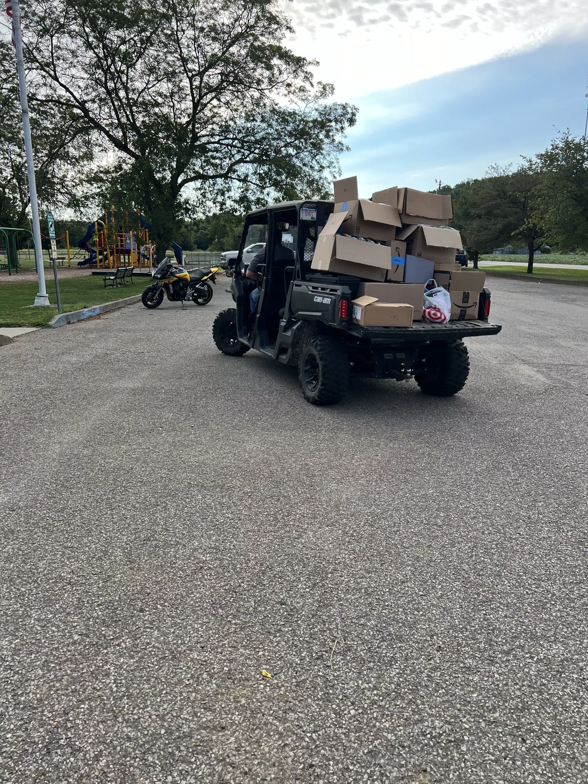 Utility vehicle loaded with cardboard boxes on a gravel road in a park with trees and lawn