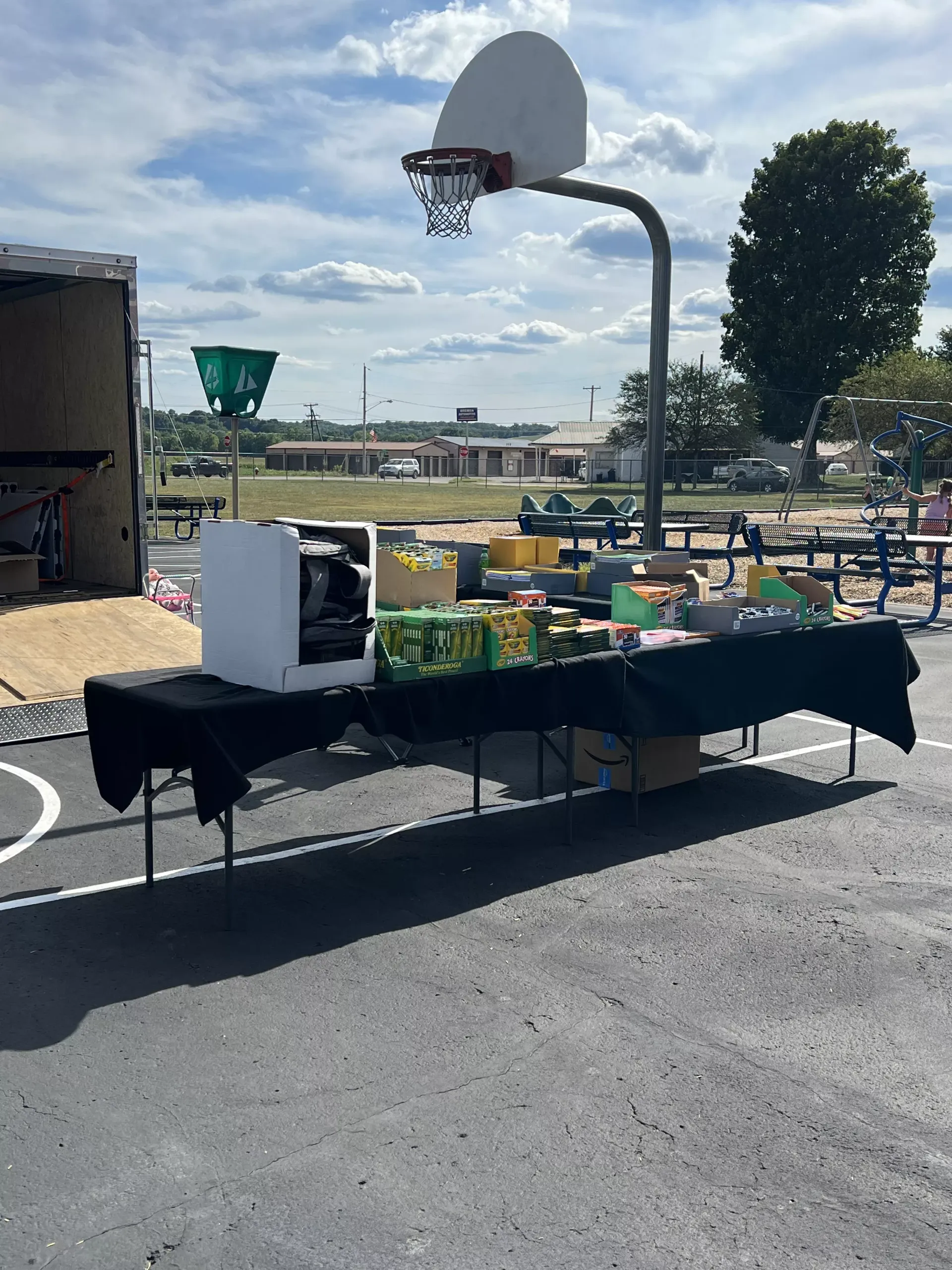 Outdoor food table with drinks and snacks set up on a basketball court near a hoop