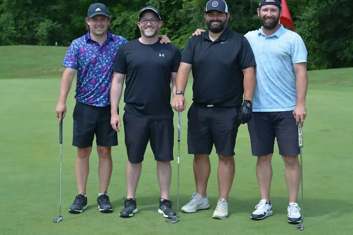 Four men standing on a golf course, smiling and posing for a group photo.