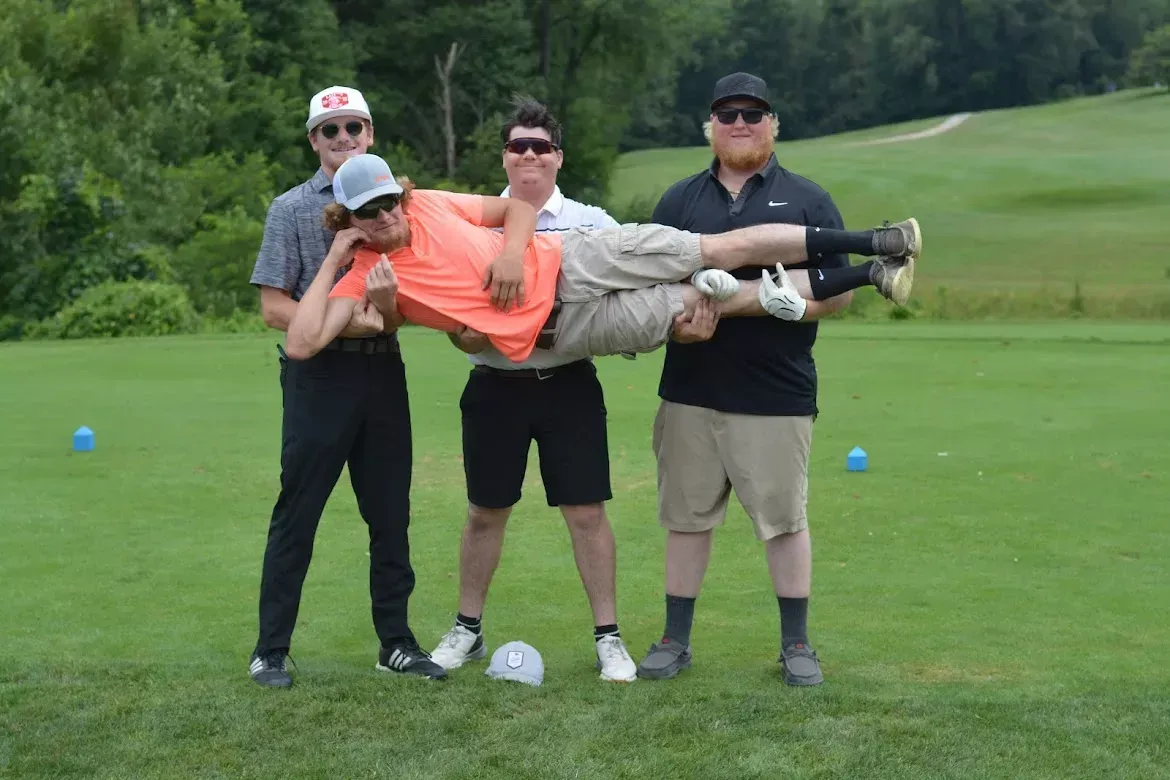 Three people carrying a person horizontally on a golf course lawn