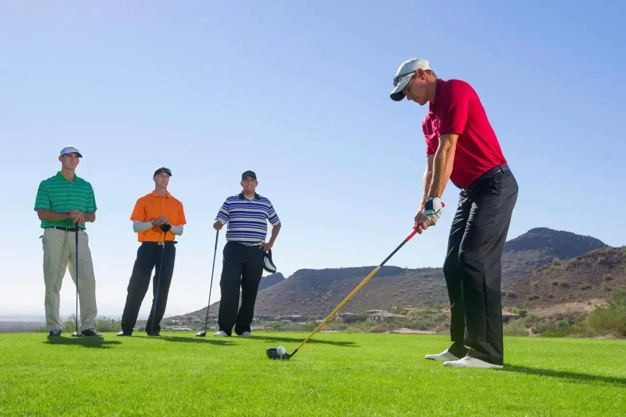 Golfer in red shirt putting on green while three people watch on a sunny course