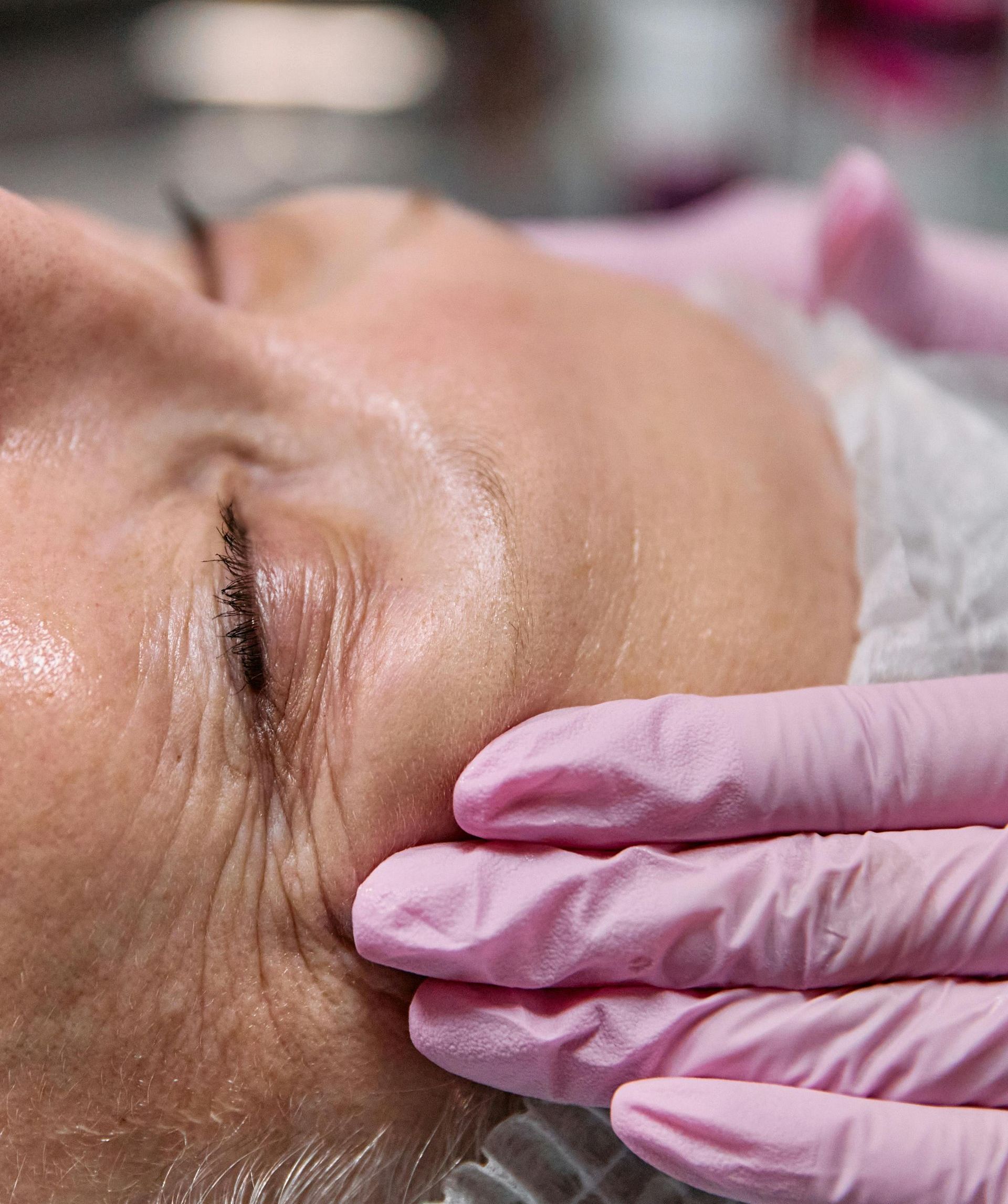 Una mujer está recibiendo un tratamiento facial con guantes rosas en la cara.
