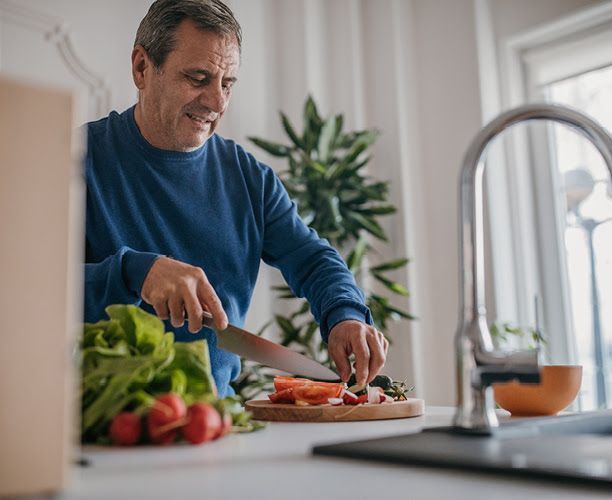 A man is cutting vegetables on a cutting board in a kitchen.