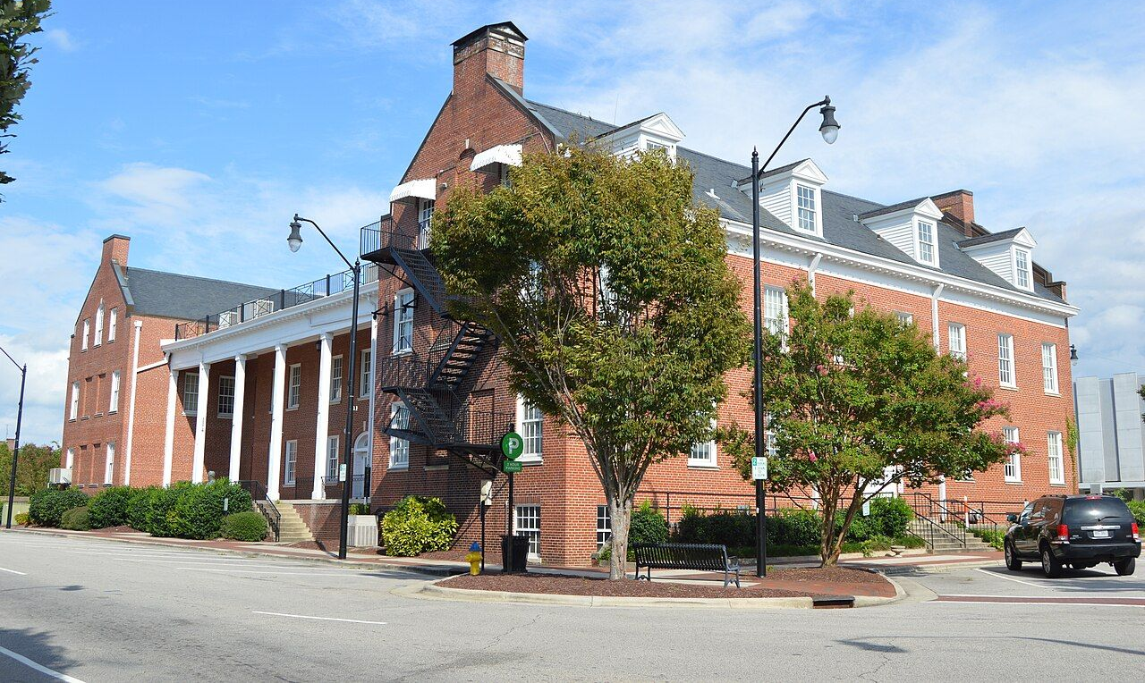A three-story brick building with white columns and a black fire escape under a blue, partly cloudy sky.