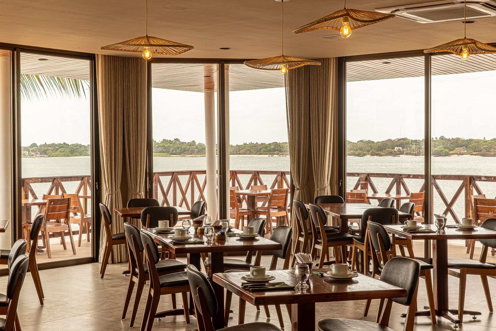 Prédio de dois andares com varandas de madeira e um carro vermelho na frente. Pessoas na calçada.