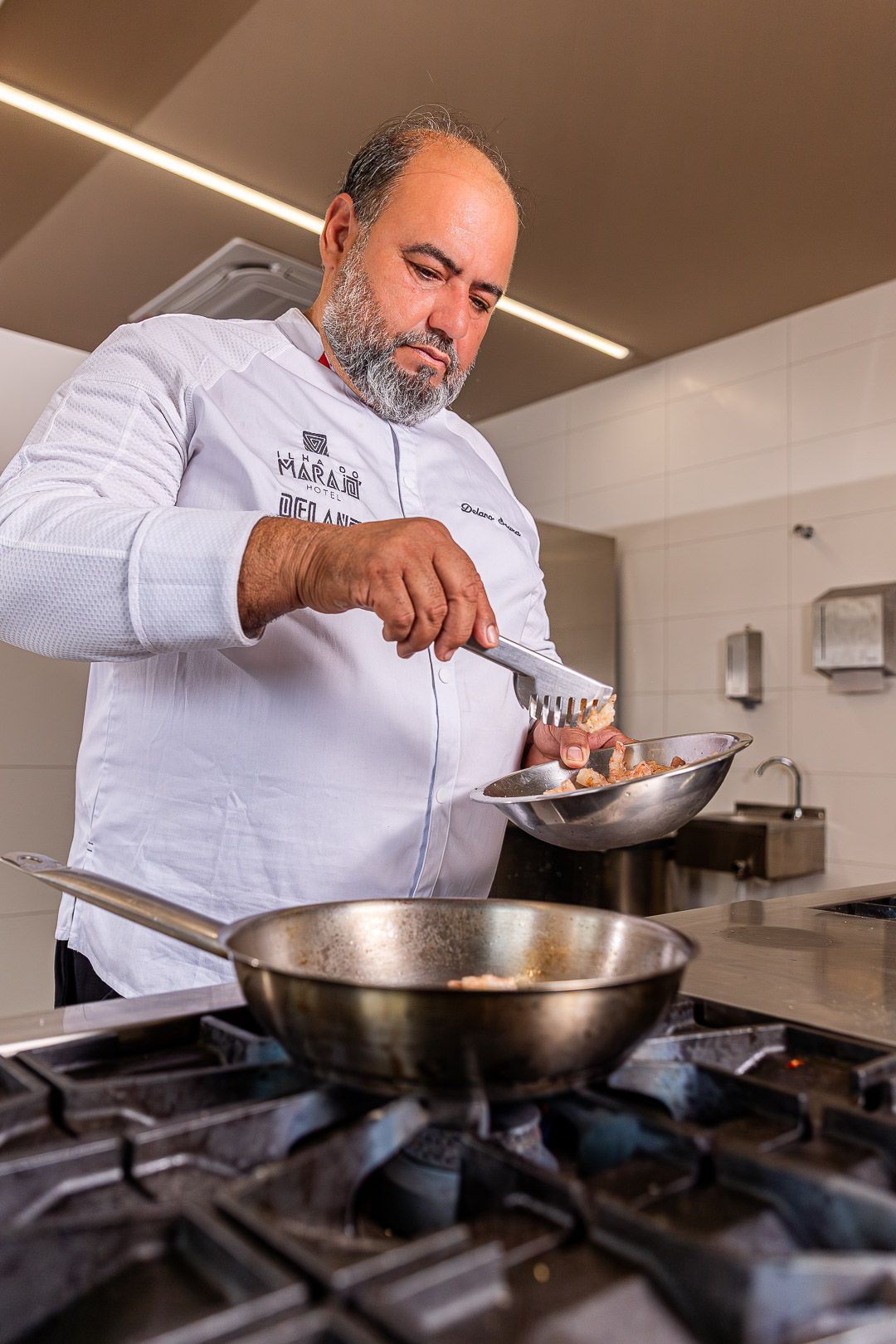 Um prédio de dois andares com um carro vermelho estacionado do lado de fora, uma ponte em primeiro plano e pessoas caminhando.