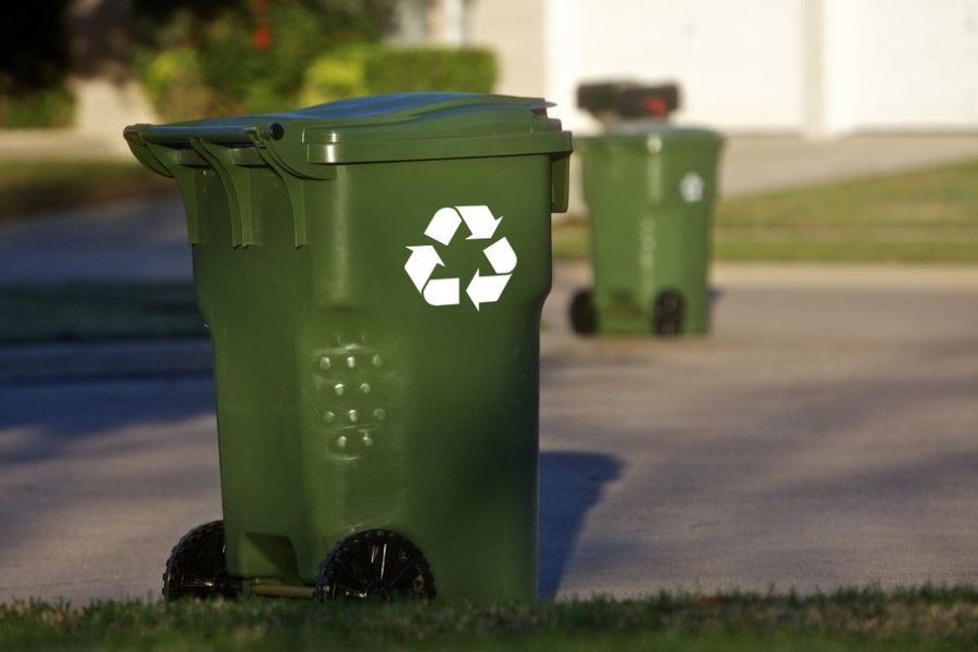 Green recycling bin with wheels and recycle symbol on a residential street. Another bin is in the background.