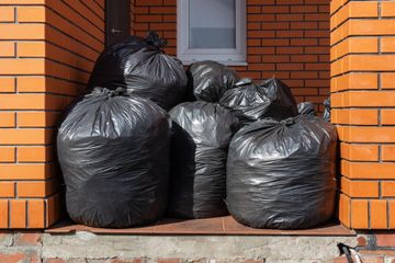 Black trash bags piled against a brick wall.