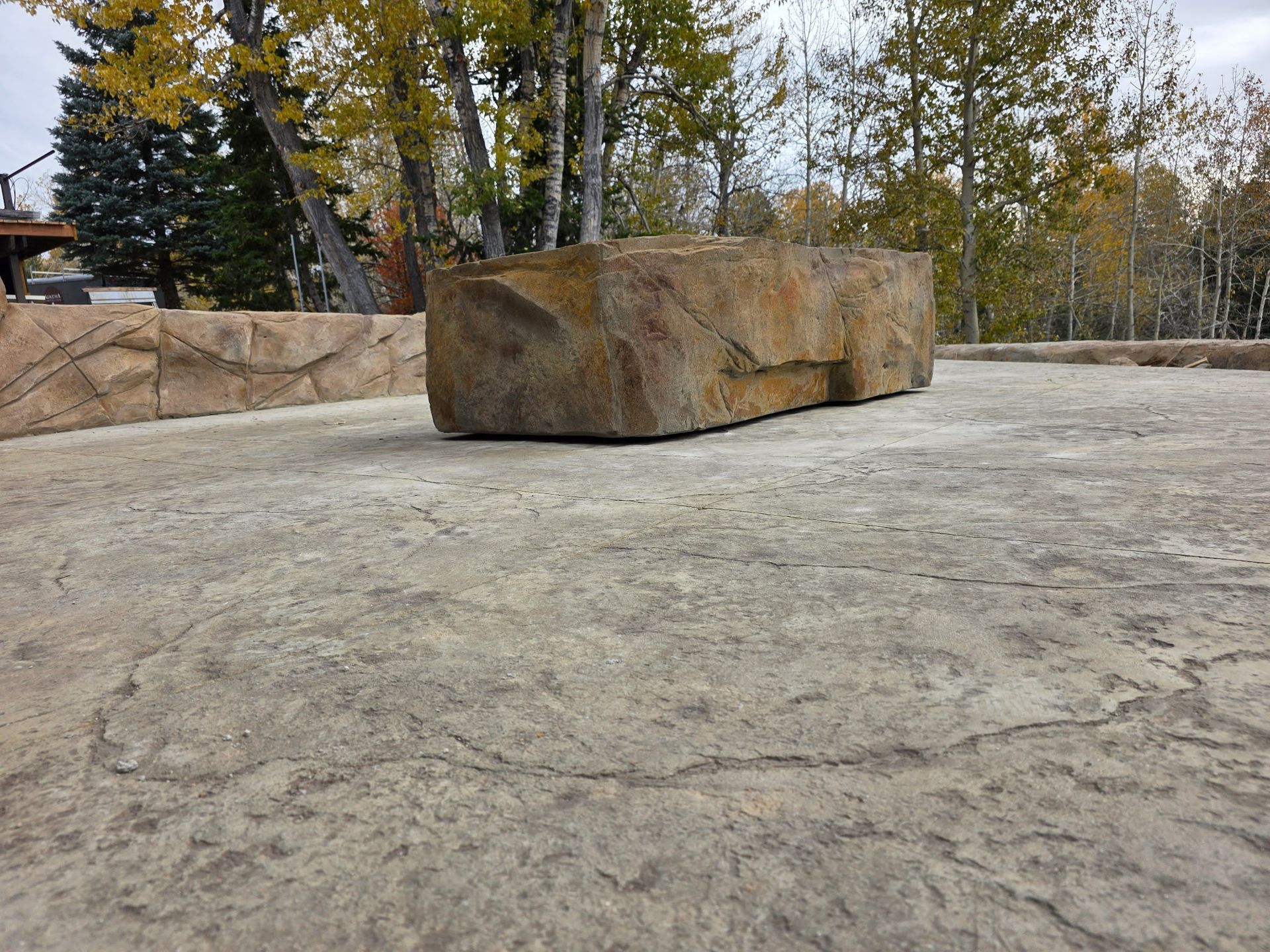 Large rectangular stone on textured concrete surface, surrounded by trees.