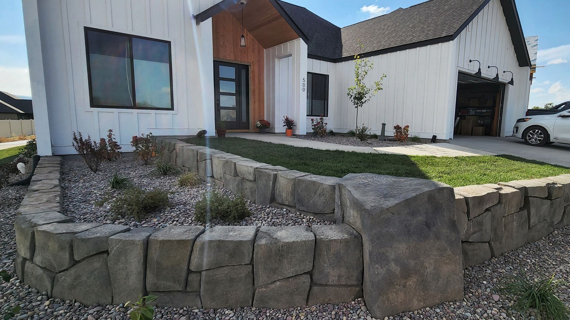 White house with stone retaining wall, front yard, and dark front door.