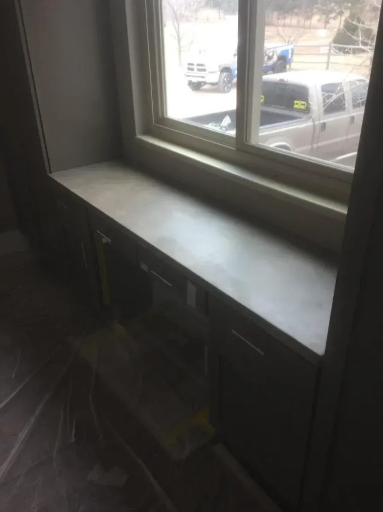 Window seat with built-in cabinetry. Gray countertop and window frame, view of vehicles outside.