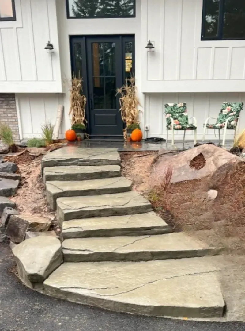 Stone steps leading to a white house with a black door, flanked by pumpkins and fall decorations.