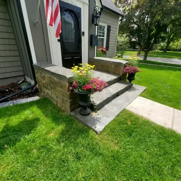 Stone steps leading to a house entrance with potted flowers and a US flag.