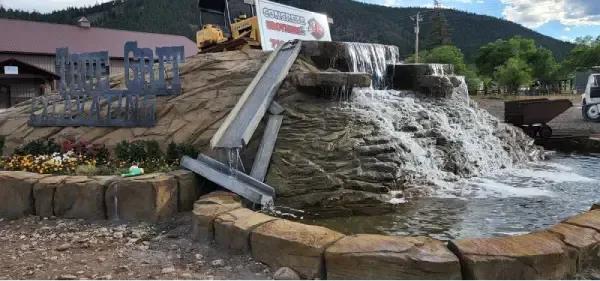 A decorative waterfall with a water sluice, surrounded by a stone border.  A mountain is in the background.