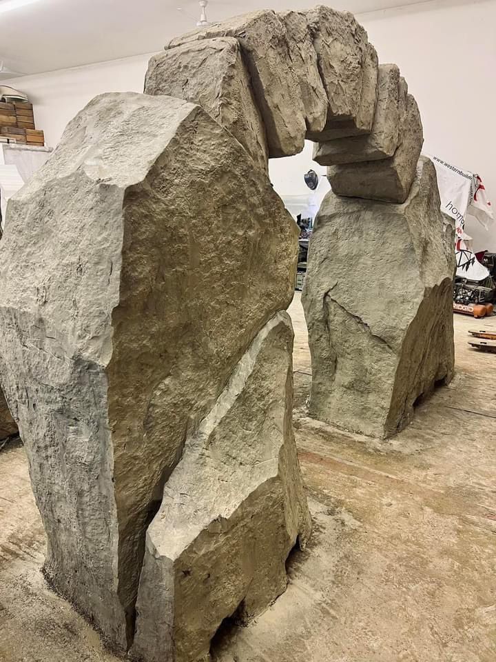 Stone archway structure made of large, textured gray blocks on a concrete floor.