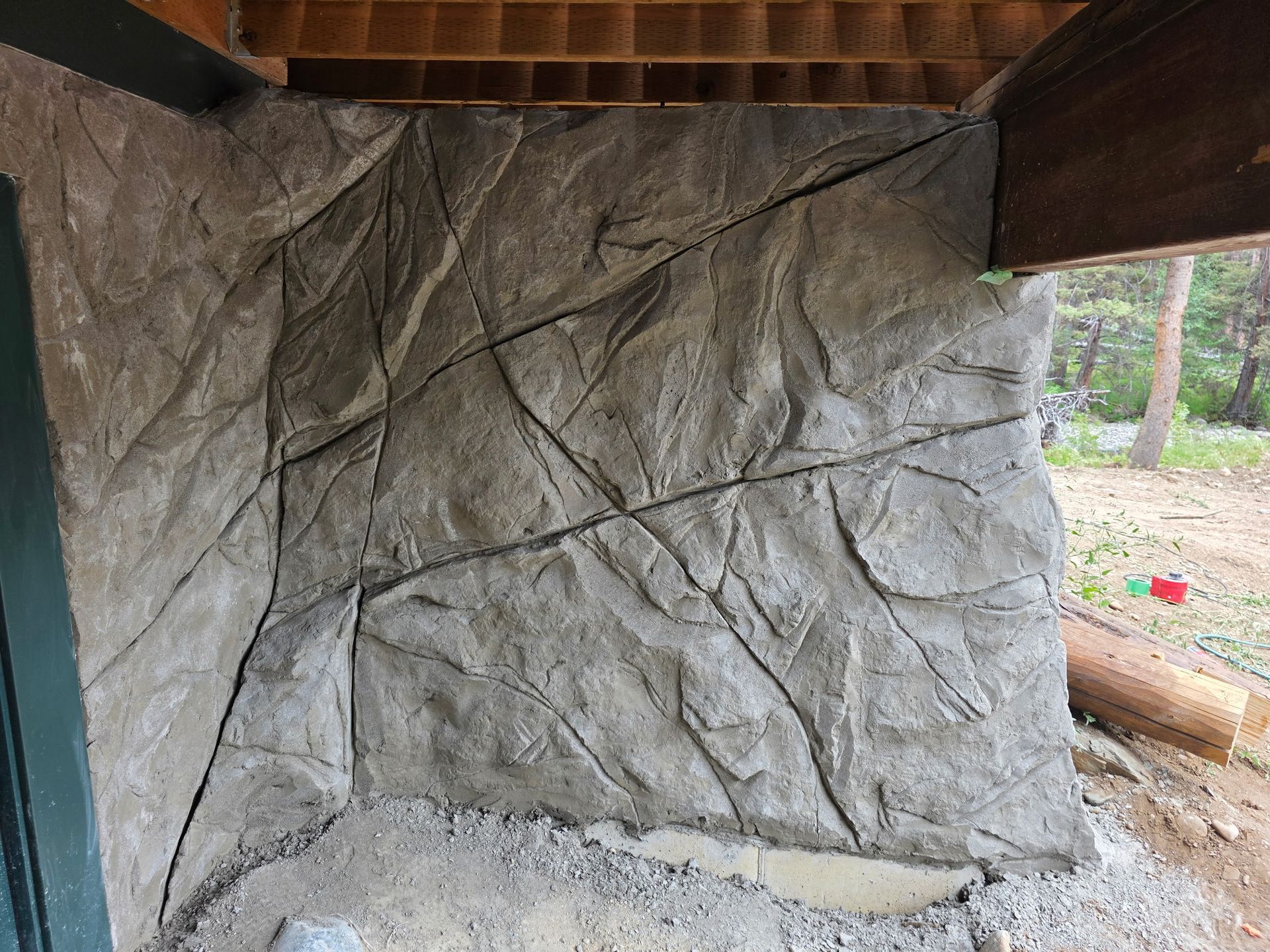 Gray concrete wall with rock-like texture and dark cracks under a wooden structure.