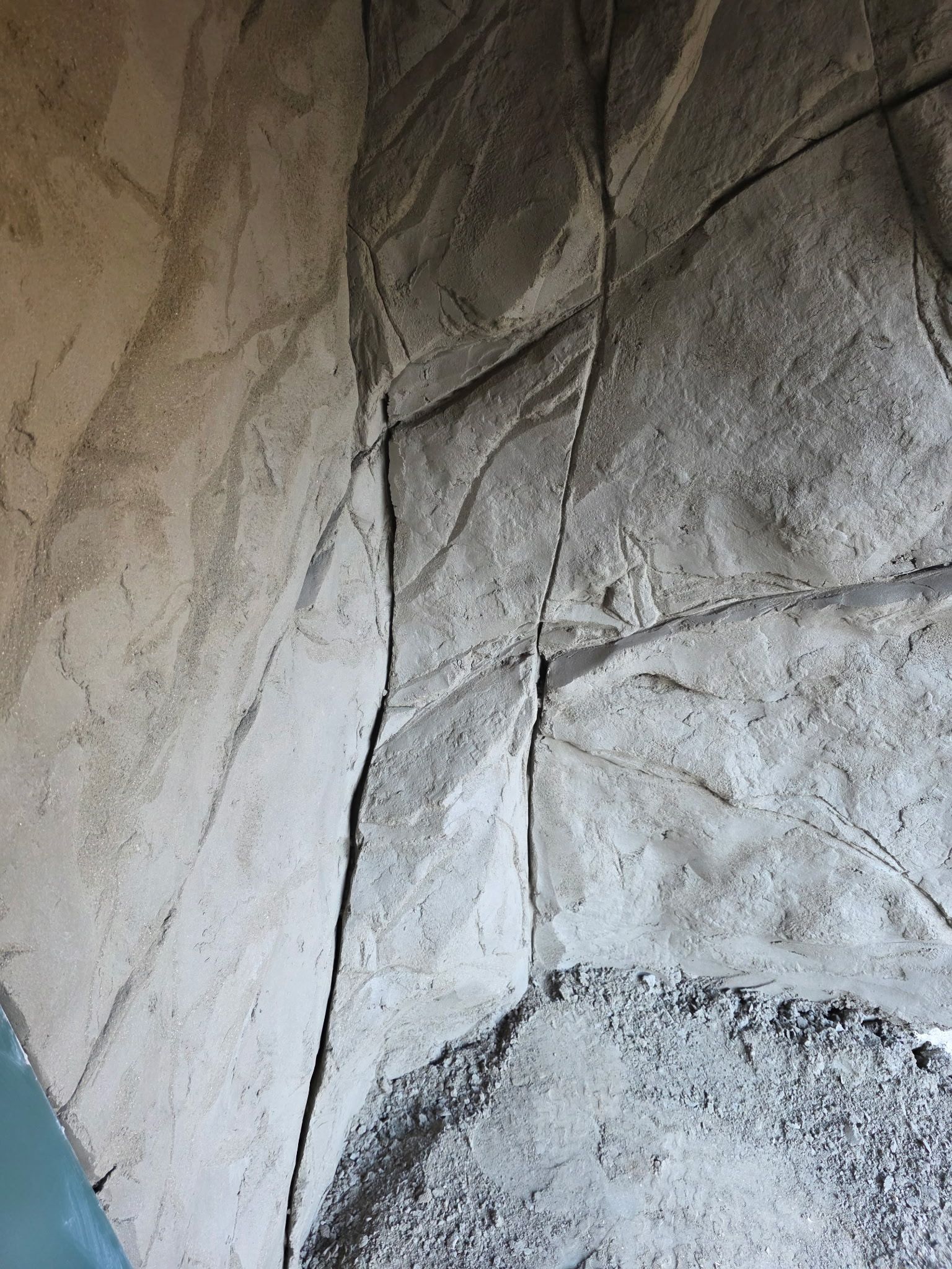 Textured wall resembling stone, light and dark gray. Cracks and crevices suggest a rock formation.