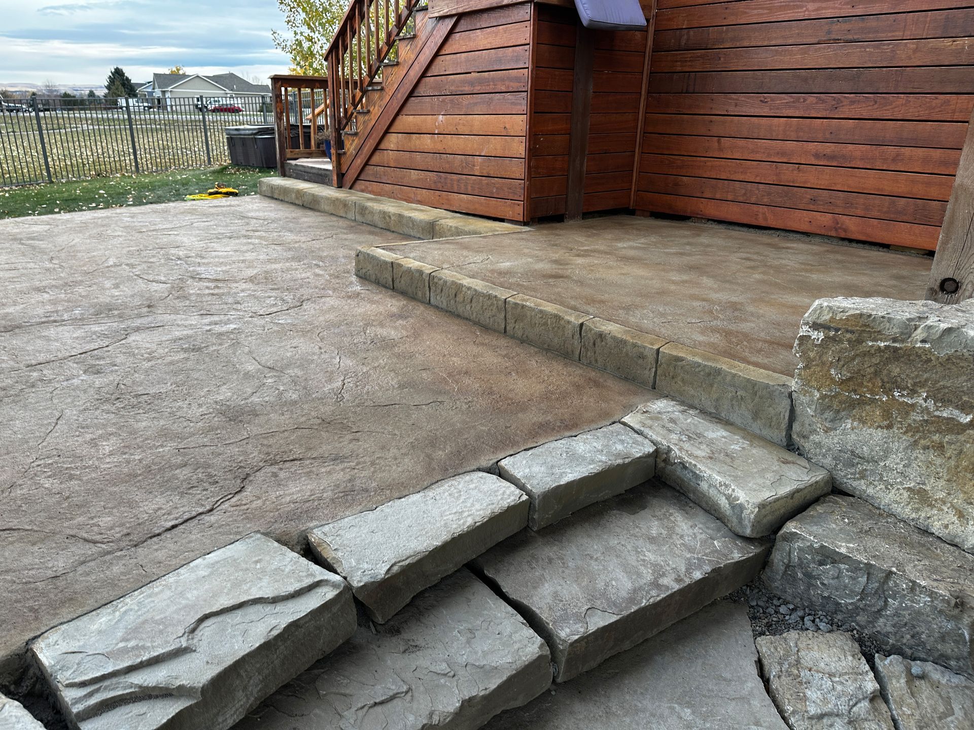 Stone steps leading to a concrete patio next to a wooden building. Overcast day.