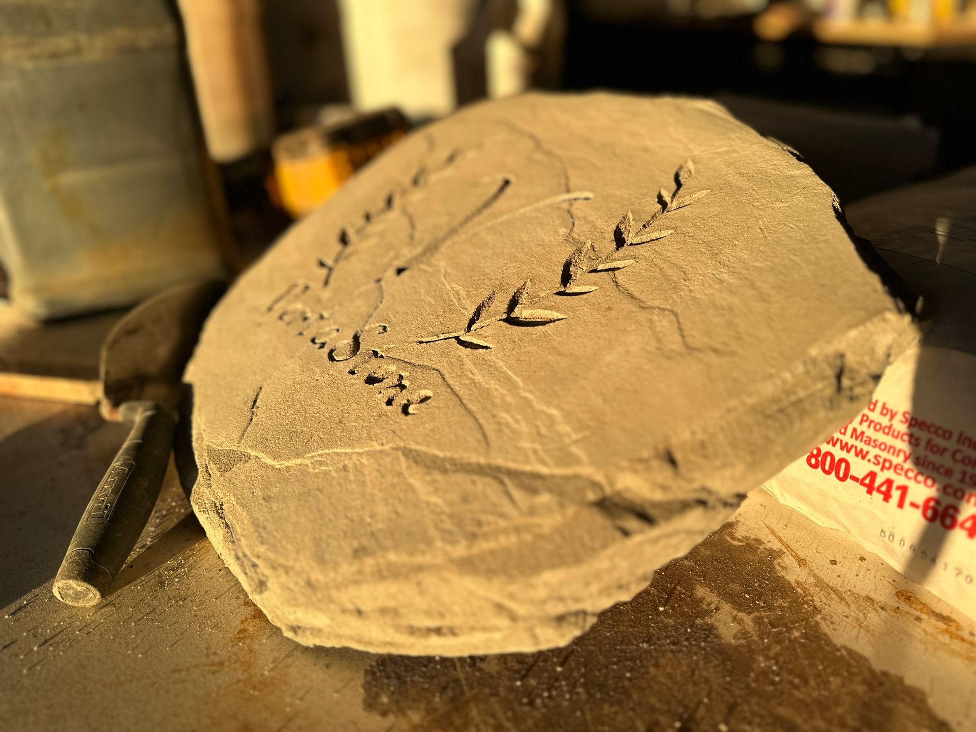 Stone carving with leaf design and inscription, outdoors, sunny.