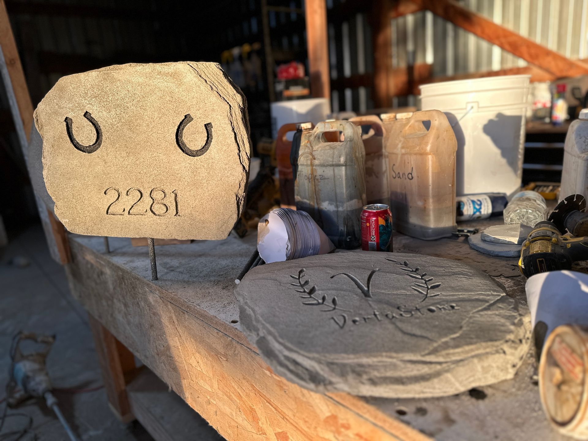 Stone signs with house numbers, horseshoes, and leaf designs on a workbench in a workshop.