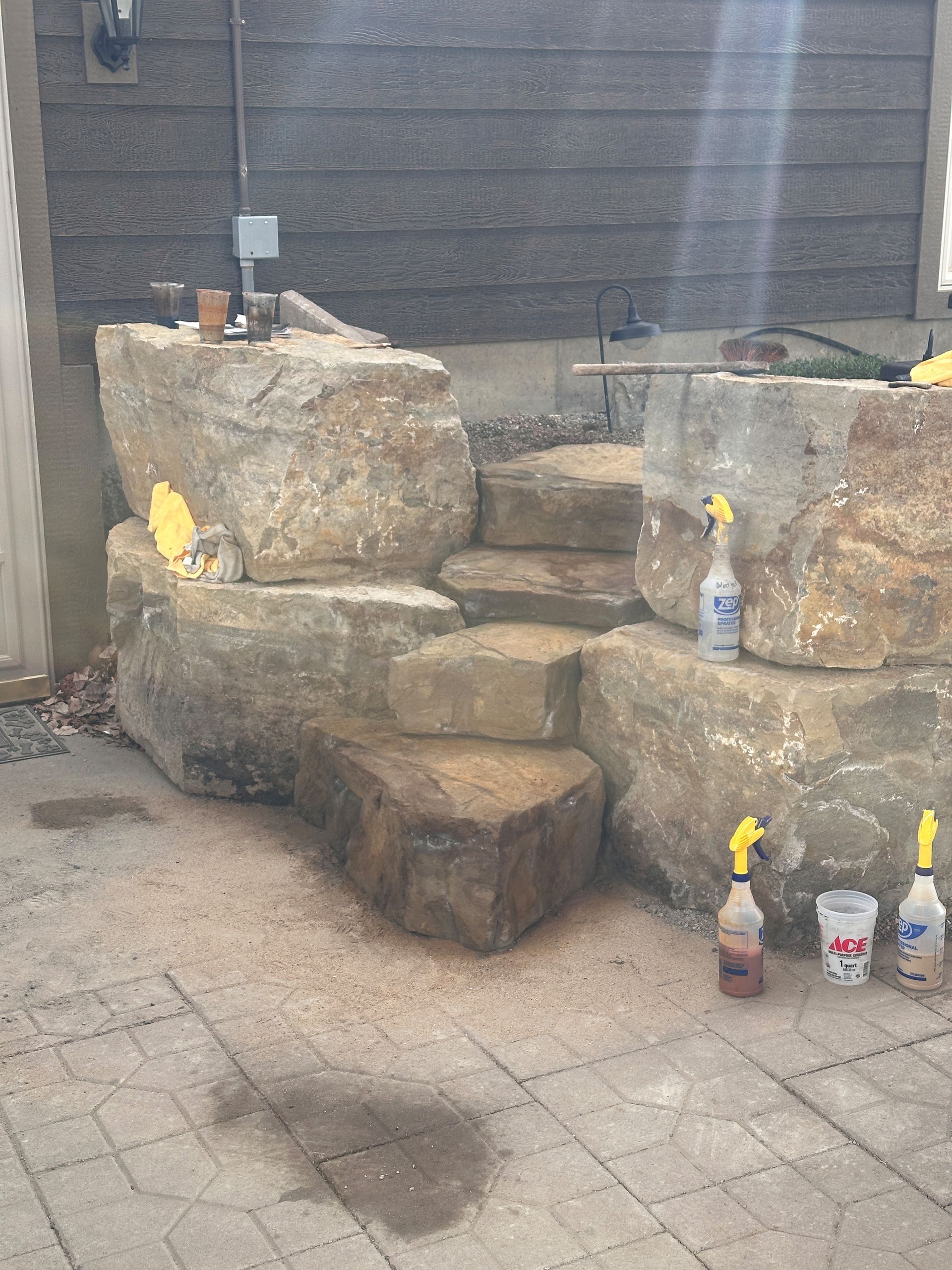 Stone steps built into a large rock formation against a wooden building. Several spray bottles are placed around.