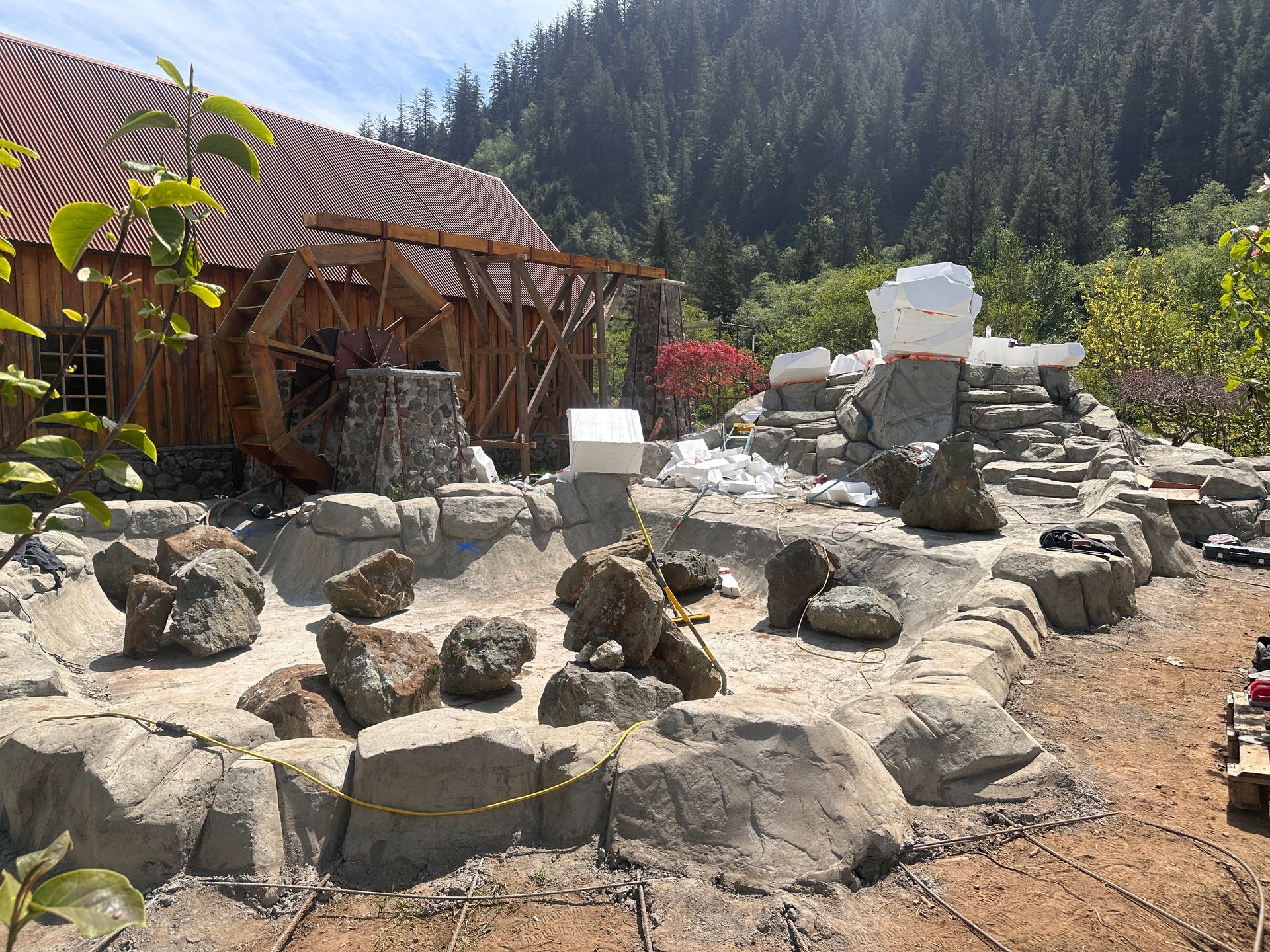 A water feature under construction with a wooden building and mountains in the background.