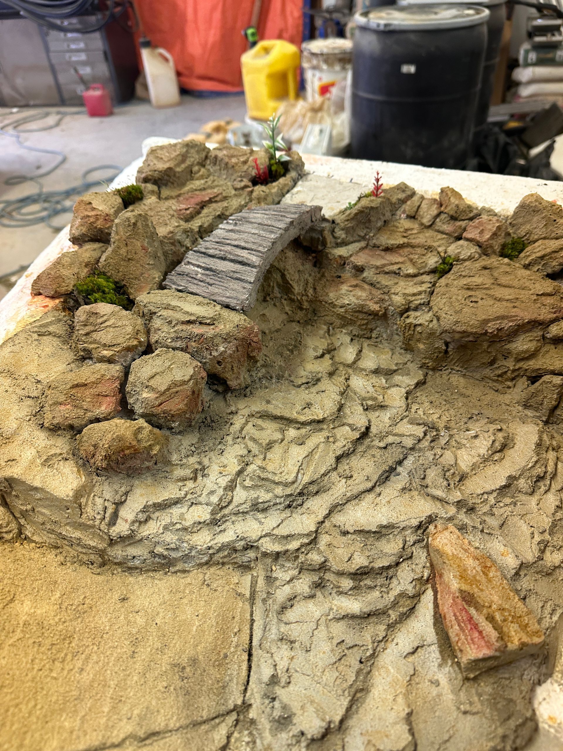 Miniature rock garden with a small stone bridge, moss, and textured surfaces.