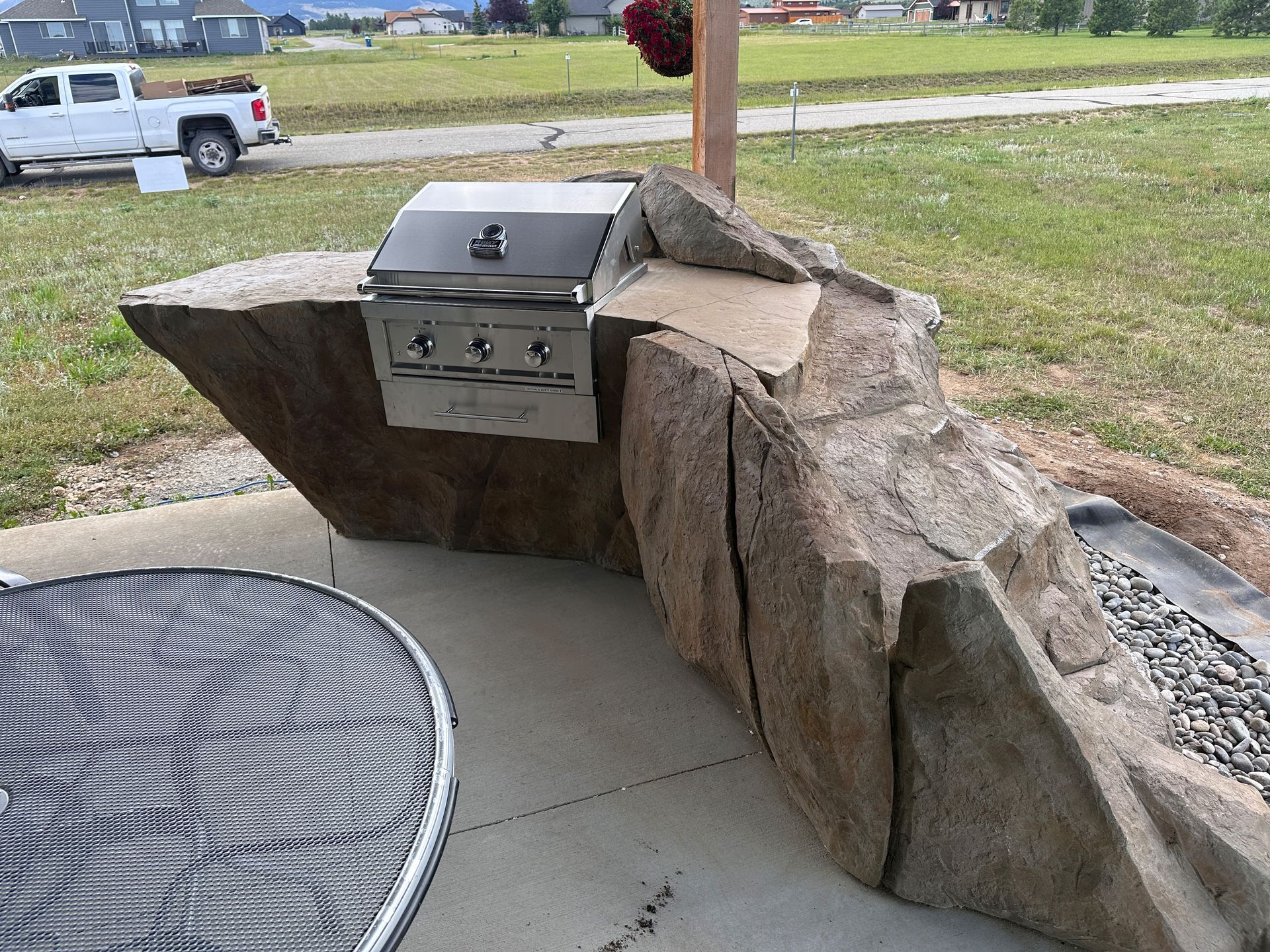 Outdoor grill station built into a rock formation, with a stainless steel grill and a fire pit.