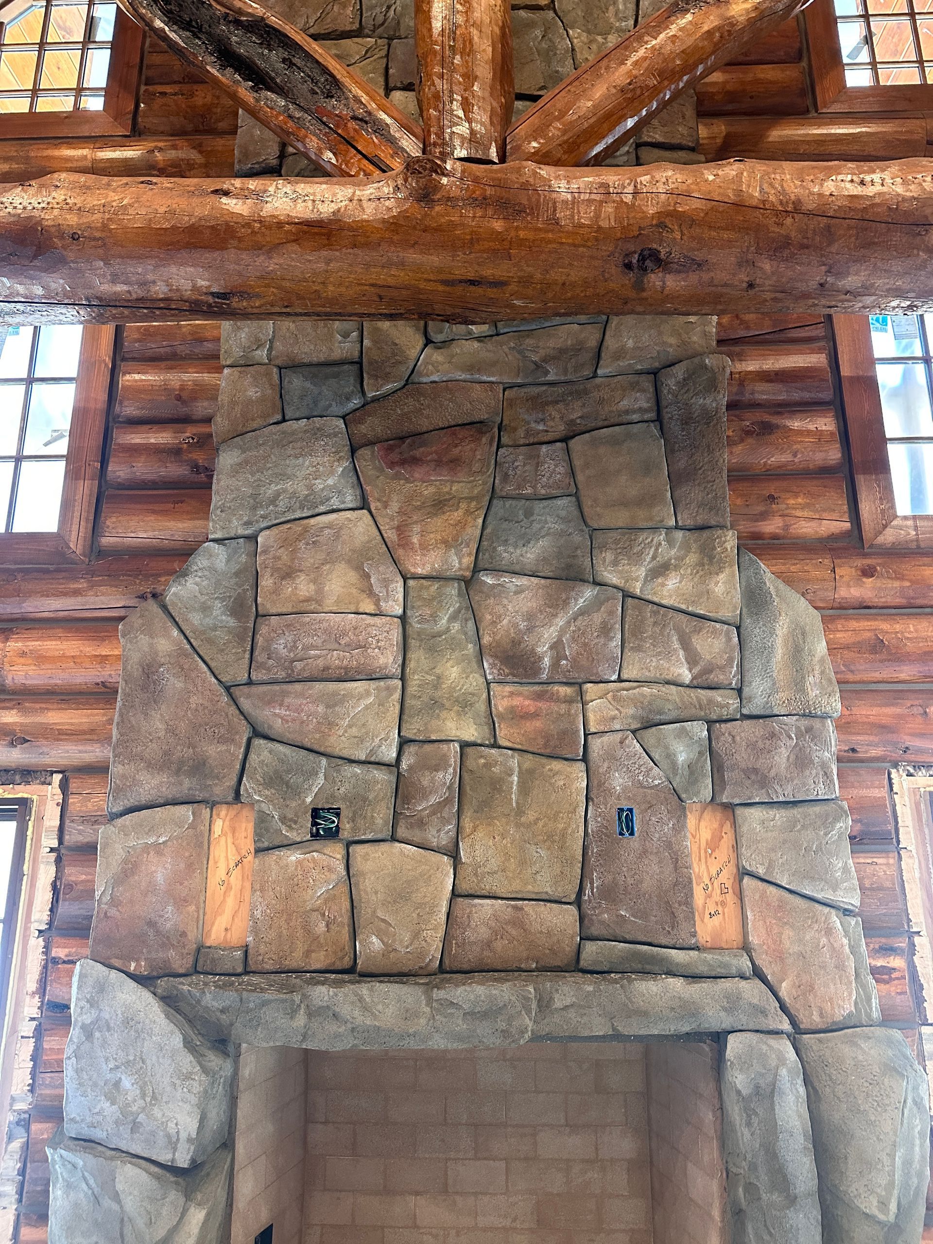 Stone fireplace in a log cabin. Brown stone with a wooden mantel and support beams.