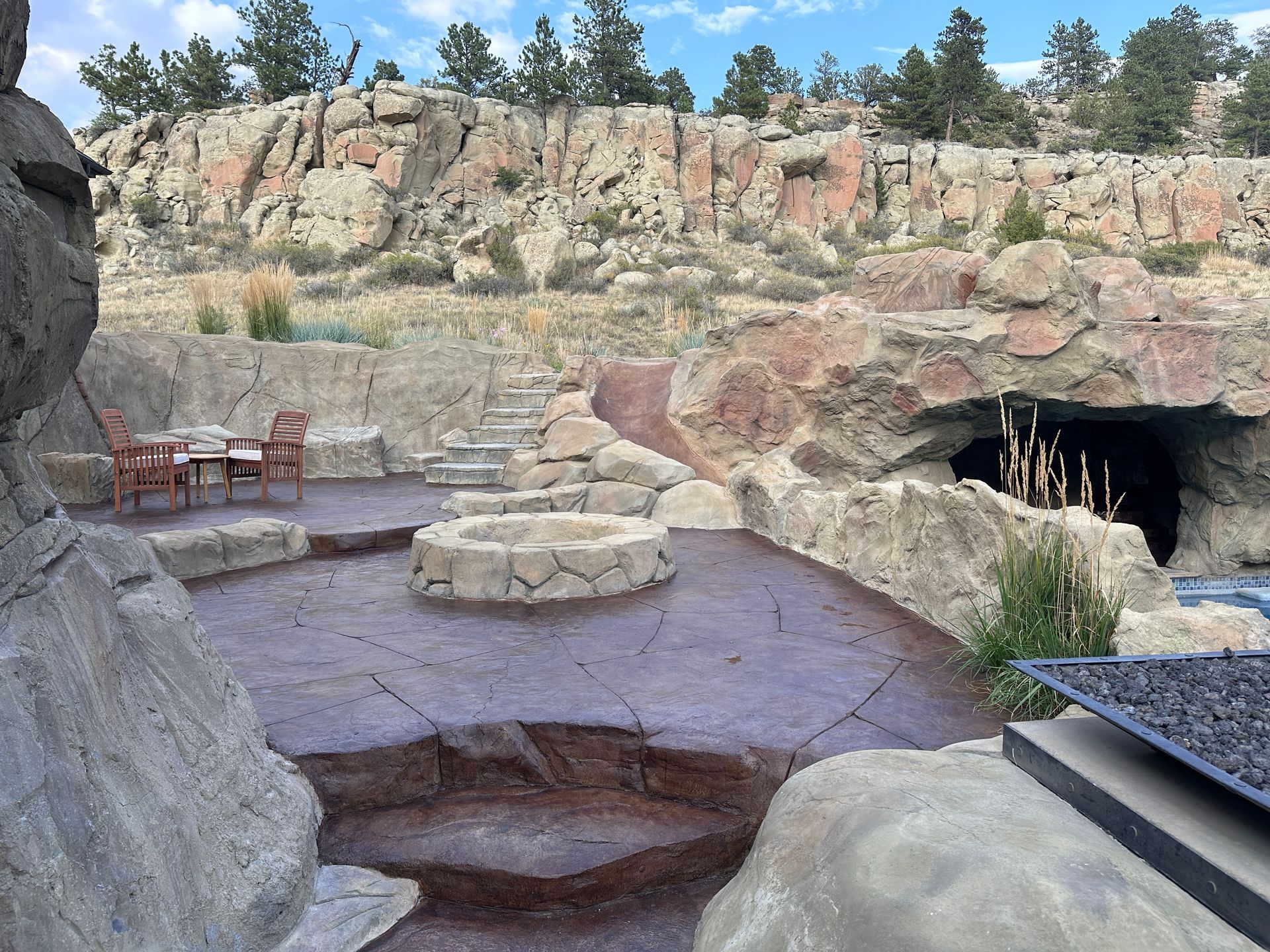 Outdoor patio with fire pit, seating, and rocky backdrop.