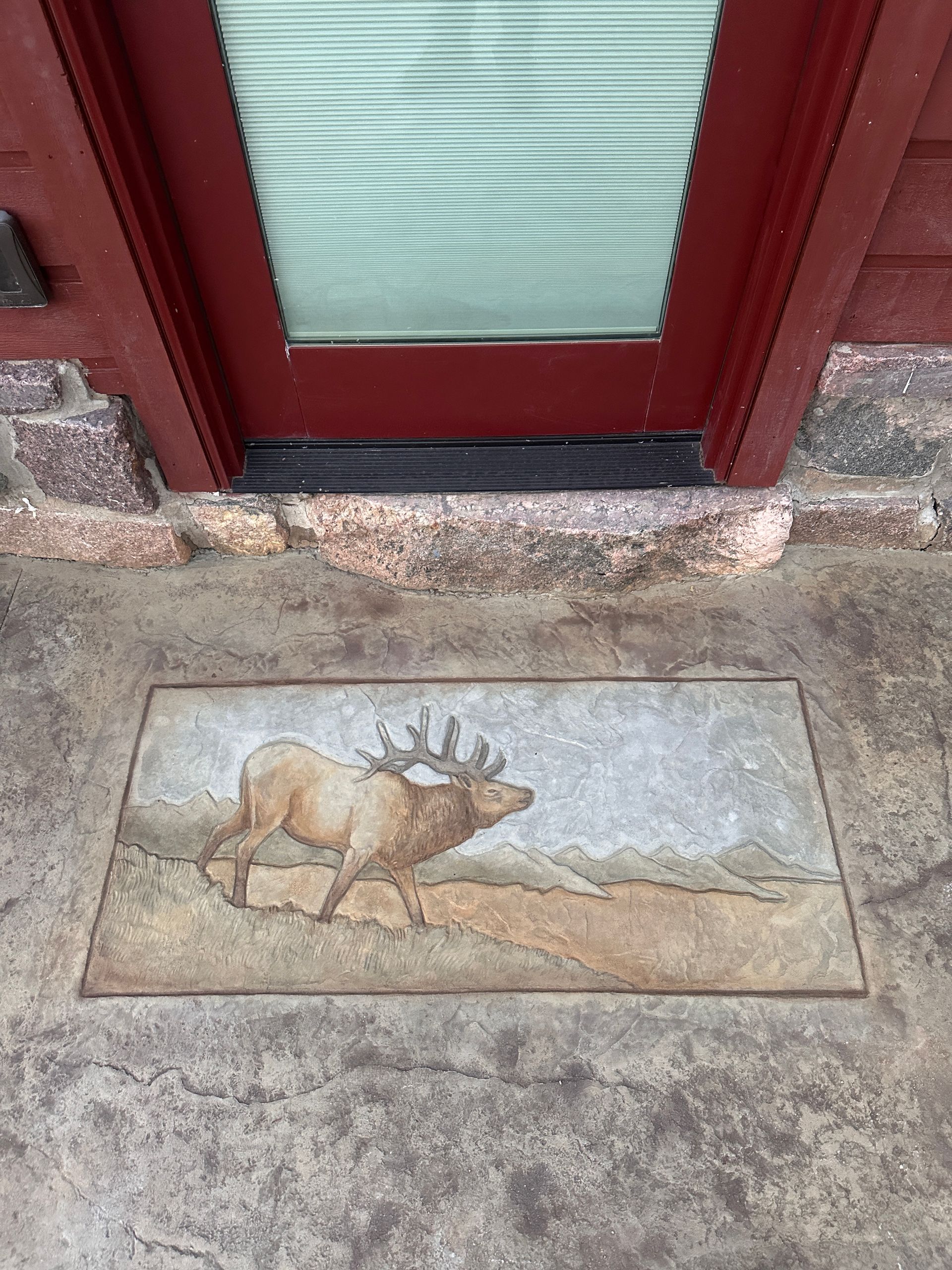 Elk stepping on a decorative stone mat in front of a red door.